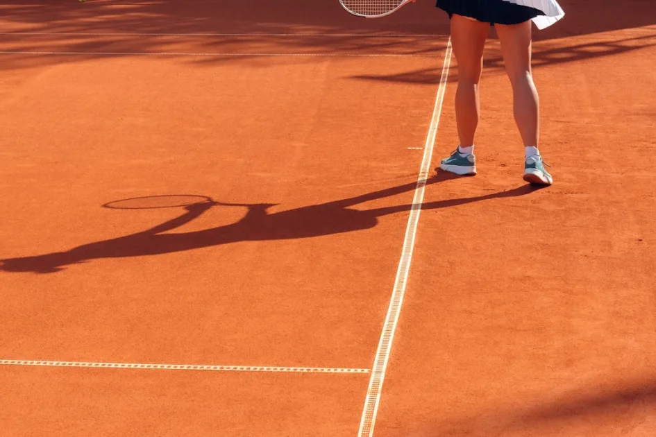 Tennis player on a clay court with long shadow